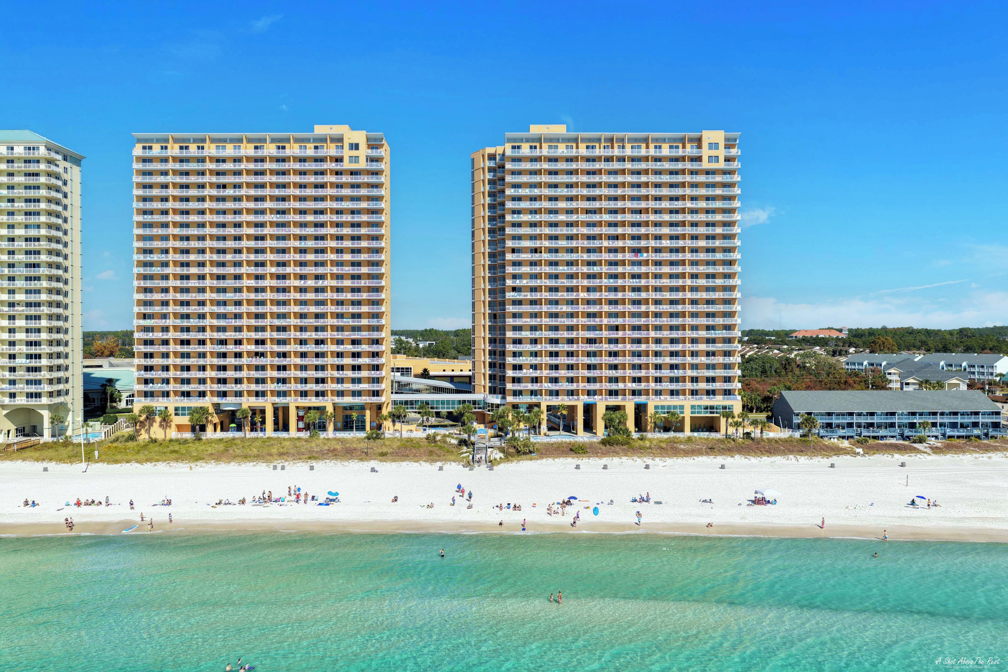 A beachfront hotel with multiple high-rise buildings, a sandy beach, and clear turquoise waters.