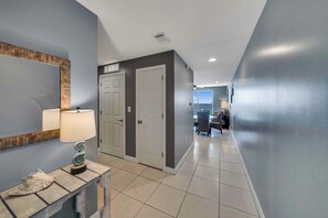 Un couloir avec un sol carrelé, un miroir fixé au mur, une lampe et une porte.