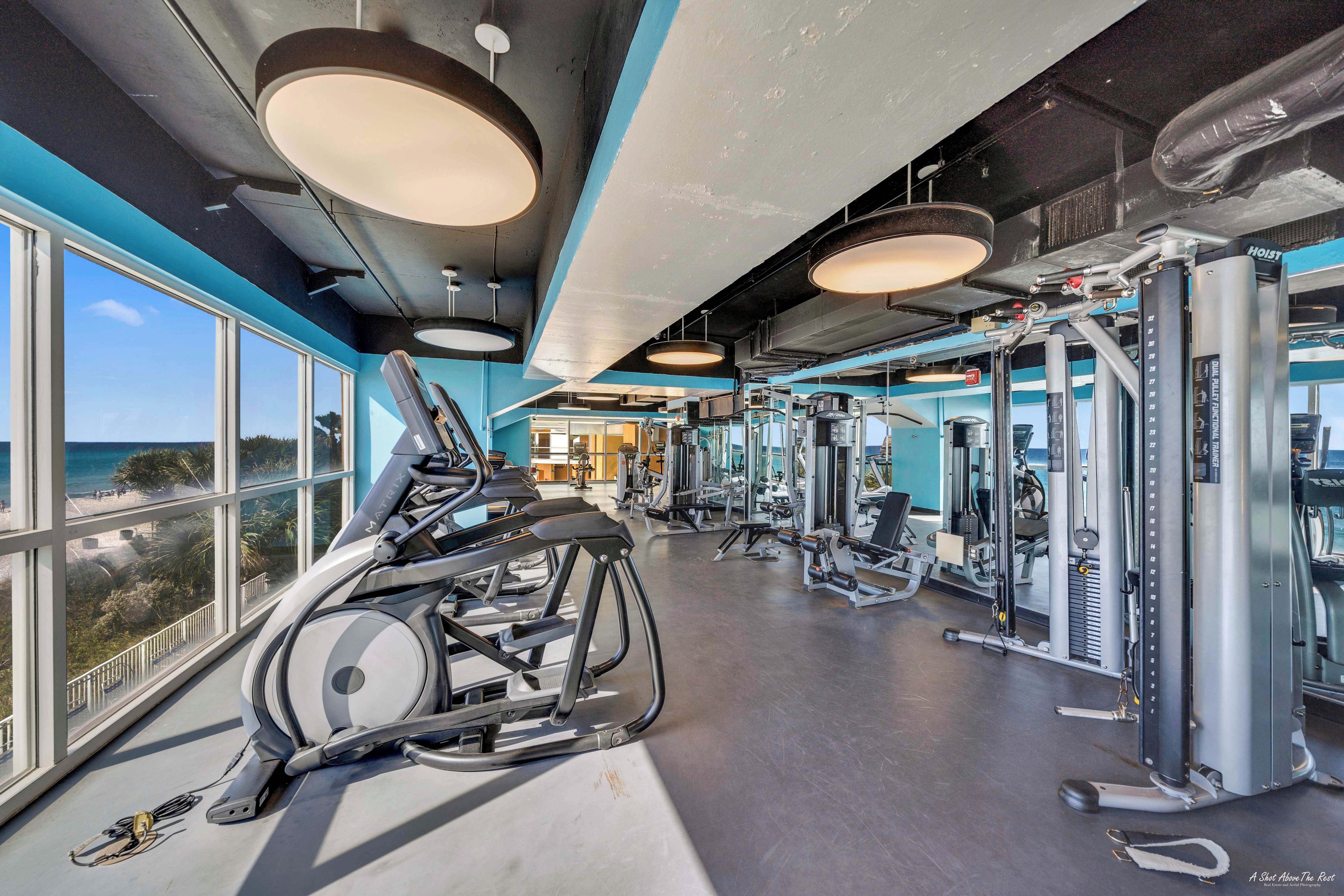 A gym with exercise equipment, large windows, and a view of the ocean.
