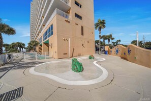 A modern building with balconies, a courtyard with a frog sculpture, palm trees, and a clear blue sky. - NEW Listing! FREE Daily Golf&Perks! Splash W502 w/Hot Tub & Heated Pool &Gym! (Panama City Beach)