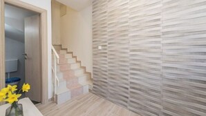 A modern interior with a staircase, a wall with a textured pattern, and a vase with flowers on a table. - Balen House (Novalja)
