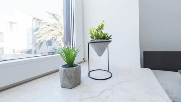 A modern room with a large window, a marble floor, a grey bed, and a small table with a potted plant. - Balen House (Novalja)
