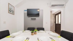 A conference room with a white table set for four, black chairs, a mounted TV, and small potted plants. - Balen House (Novalja)
