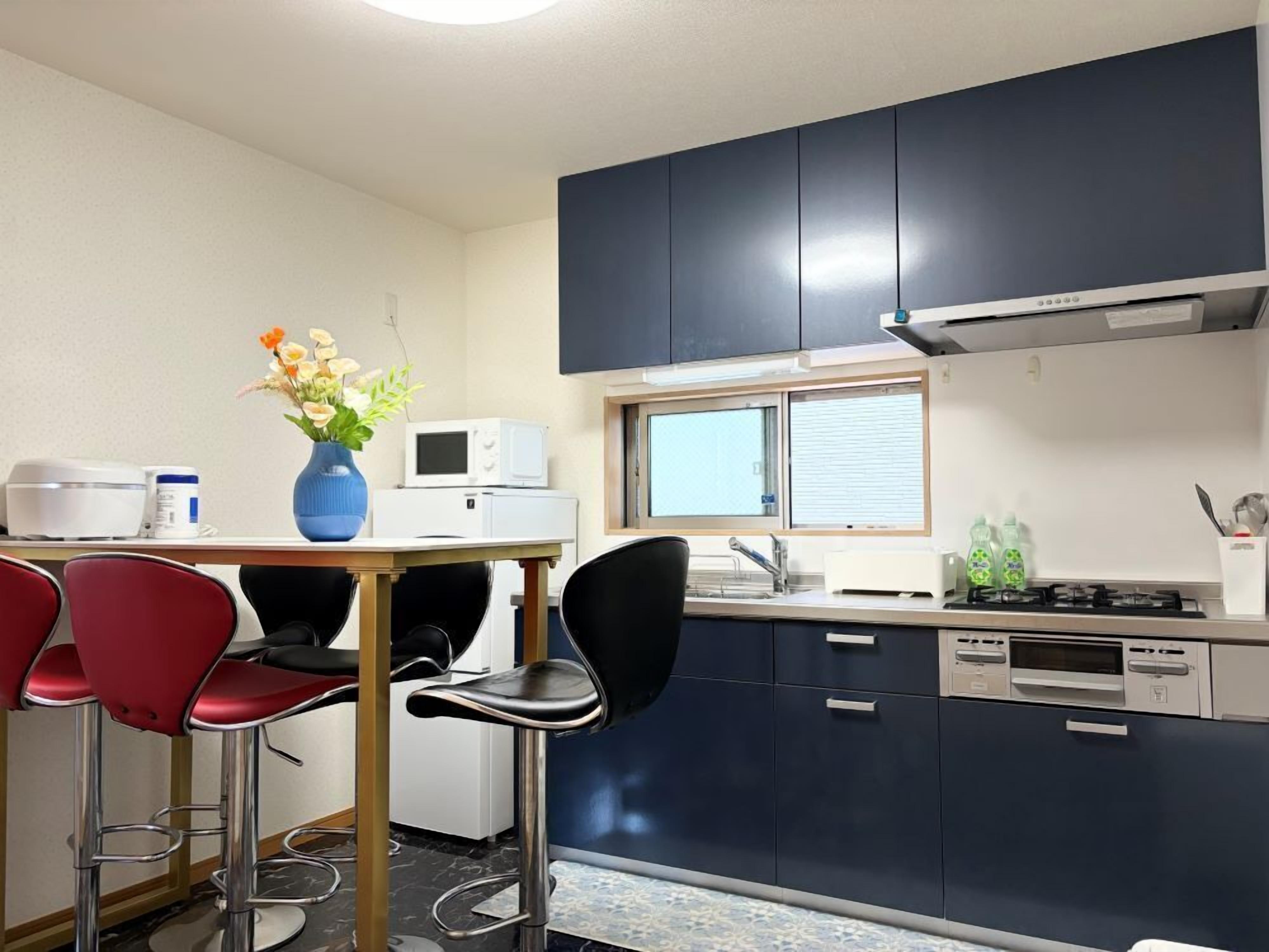 A compact kitchen with a microwave, stove, and sink. There are two red chairs and a blue vase with flowers on the table.