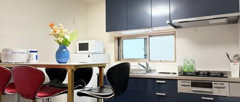 A compact kitchen with a microwave, stove, and sink. There are two red chairs and a blue vase with flowers on the table.