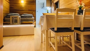 Ein gemütlicher Raum mit Holzwänden, einer hölzernen Bank mit Kissen, einem Tisch mit Stühlen und einer Vase mit Blumen.
