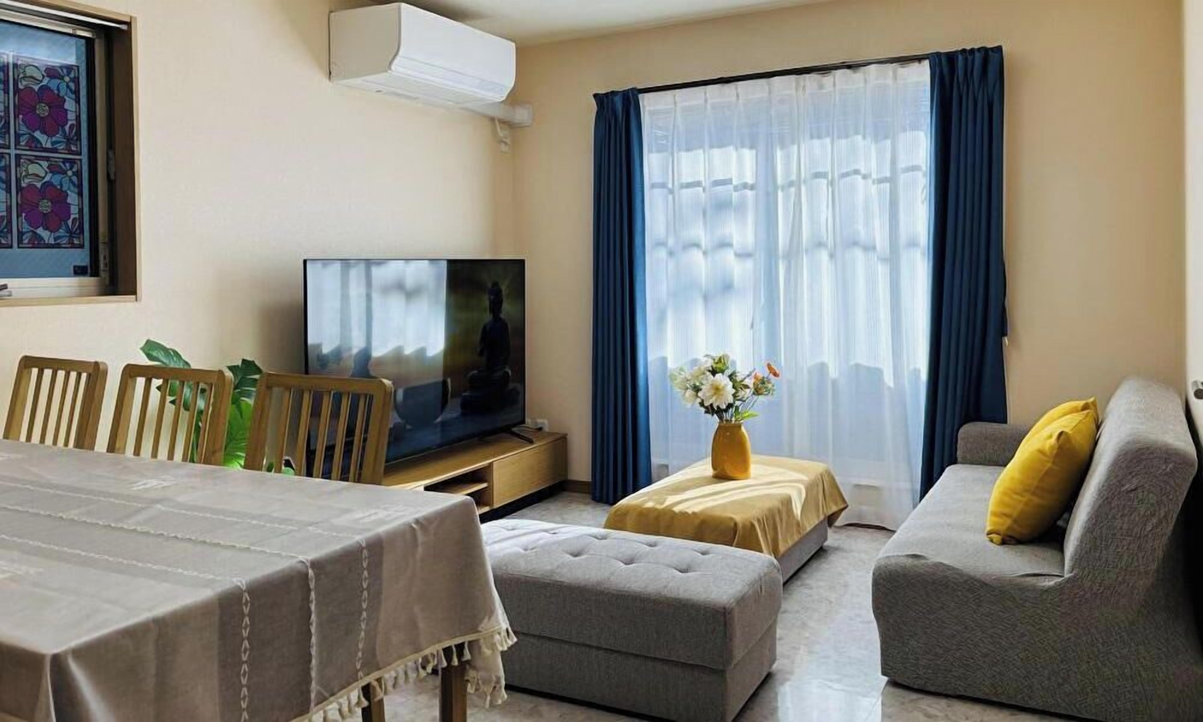 A living room with a sofa, ottoman, TV, and a dining table.