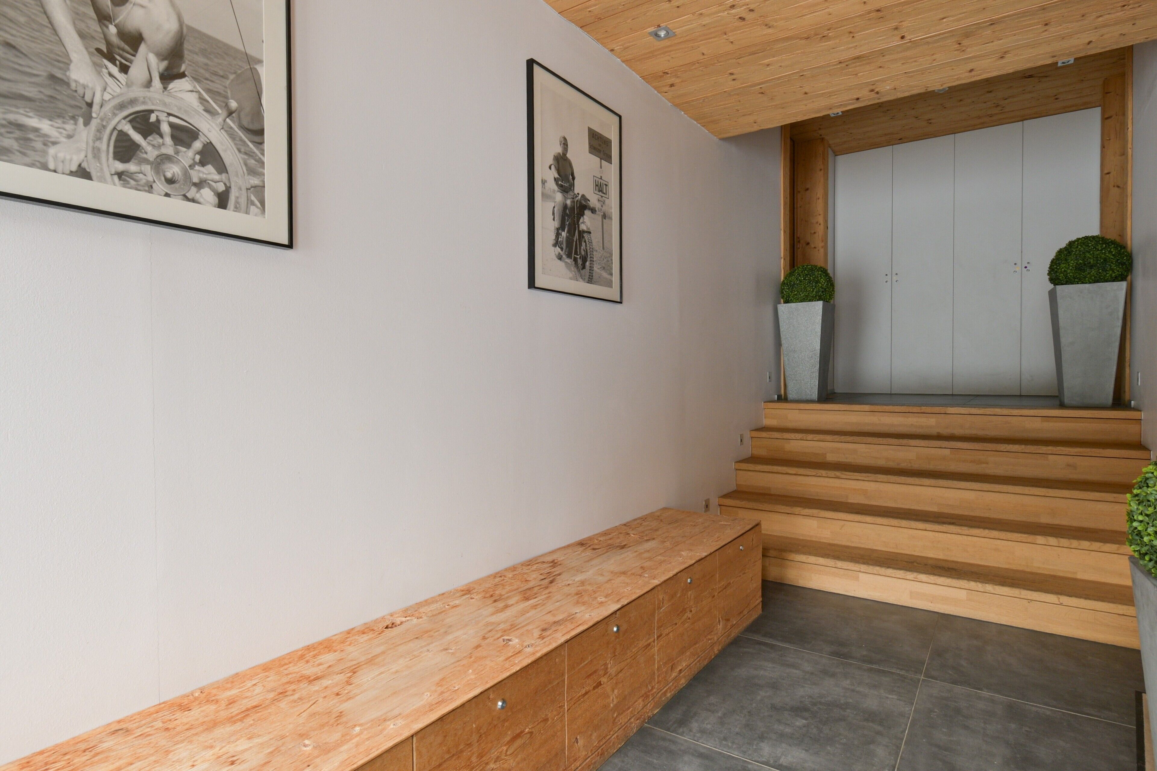 A staircase with wooden steps leading to a door, a wooden bench, and two potted plants.