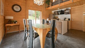 Een houten interieur met een eettafel, stoelen, een keuken en een klok aan de muur.
