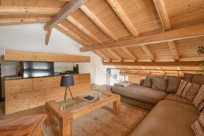 A wooden ceiling with exposed beams, a sofa, a glass coffee table, a wooden cabinet, and a television.