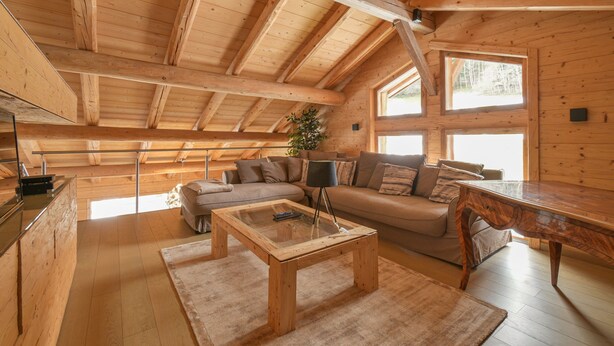 Een ruime loft met een hoge plafond, houten balken, een bank, een bijzettafeltje en grote ramen.