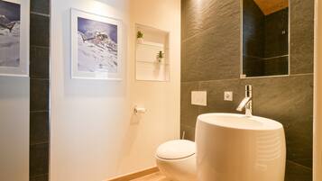 Een moderne badkamer met toilet, een ruim wastafelmeubel, een ingelijst schilderij en een klein plankje met planten.