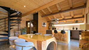 A modern kitchen with wooden beams, a spiral staircase, and a dining area with a glass table and white chairs. - Apartment 'Le Jalouvre': Mountain View, Balcony, and Wi-Fi (Saint-Jean-de-Sixt)