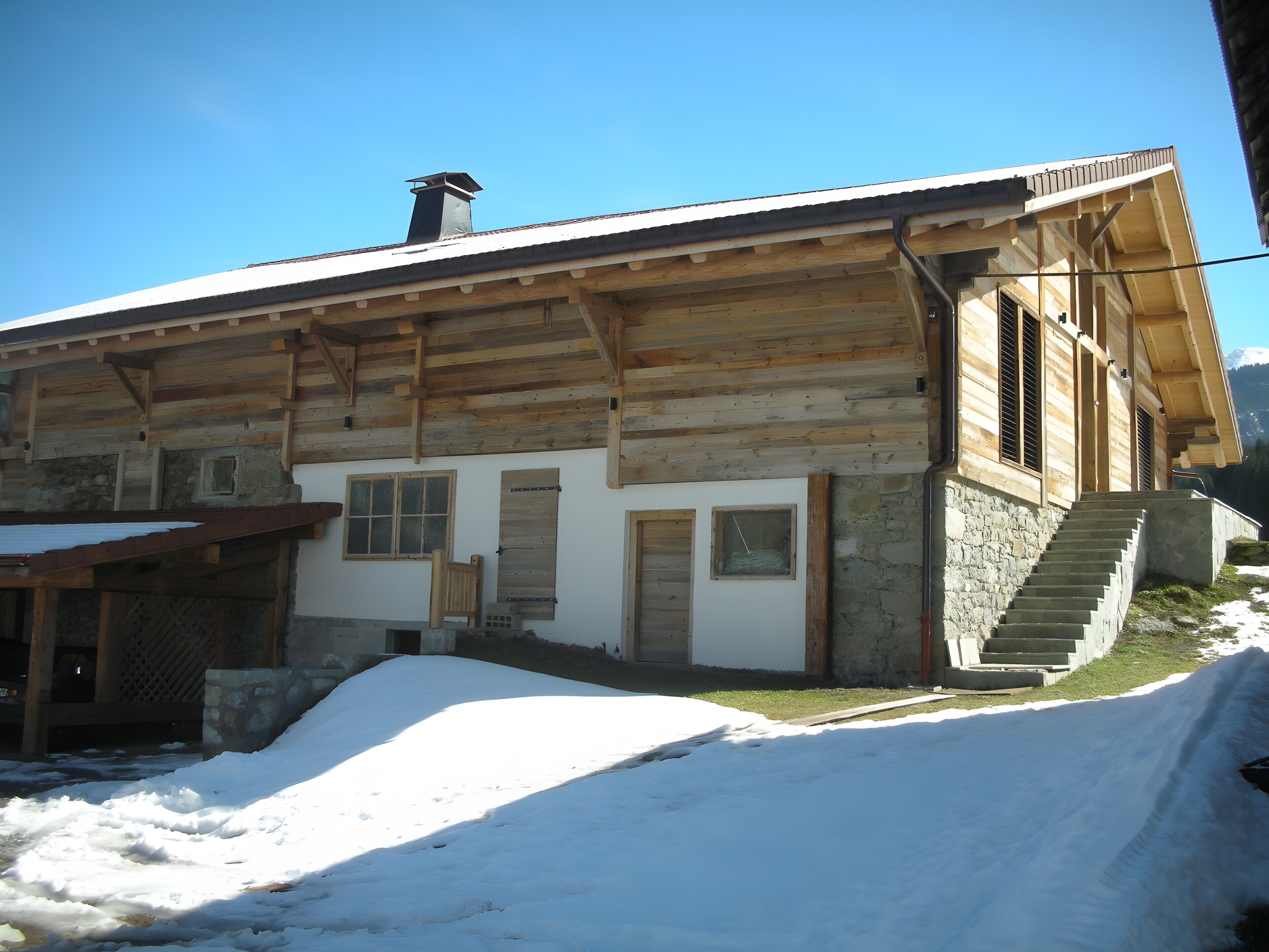 Un chalet en bois, doté de fondations en pierre, d’une cheminée et d’un escalier menant à l’entrée.