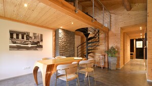 A modern interior with a wooden dining table, chairs, a spiral staircase, and a stone accent wall. - Apartment 'Le Jalouvre': Mountain View, Balcony, and Wi-Fi (Saint-Jean-de-Sixt)
