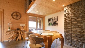 A wooden interior with a dining table, chairs, a clock, and a stone wall. - Apartment 'Le Jalouvre': Mountain View, Balcony, and Wi-Fi (Saint-Jean-de-Sixt)