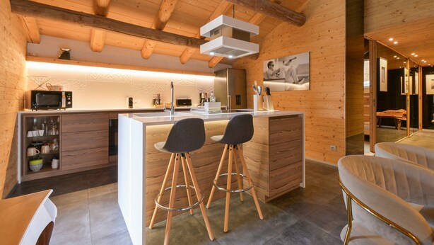 Une cuisine moderne avec des poutres en bois, un îlot central doté de tabourets et un four à micro-ondes.