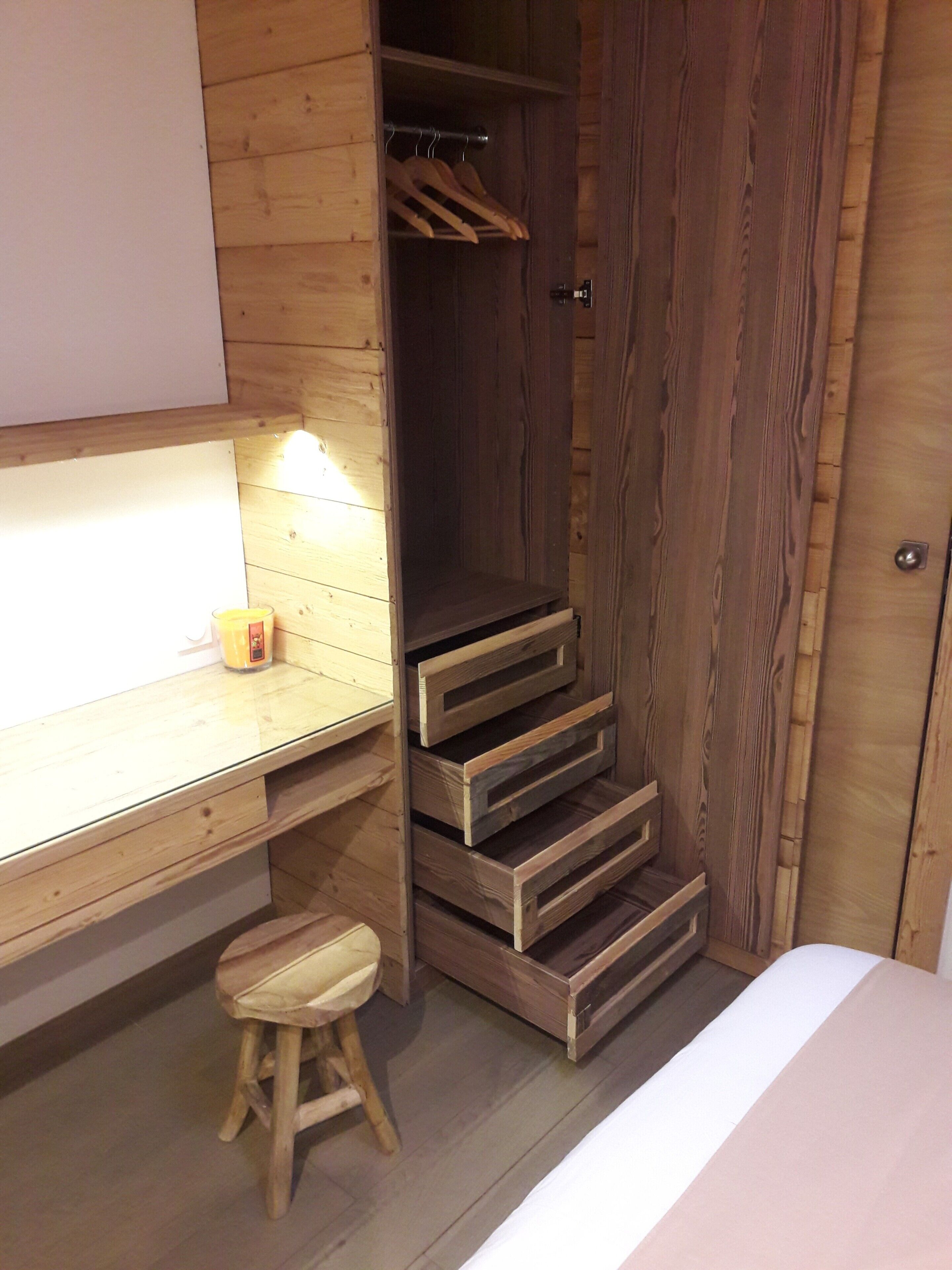 Une pièce en bois contenant un bureau, un tabouret, une armoire et un lit.
