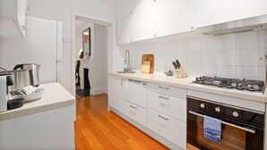 A modern kitchen with white cabinetry, a wooden floor, a gas stove, and a dishwasher. - Stylish 2-bed House With Private Courtyard (Sydney)