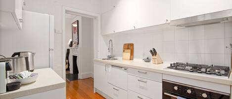 A modern kitchen with white cabinetry, a wooden floor, a gas stove, and a dishwasher.