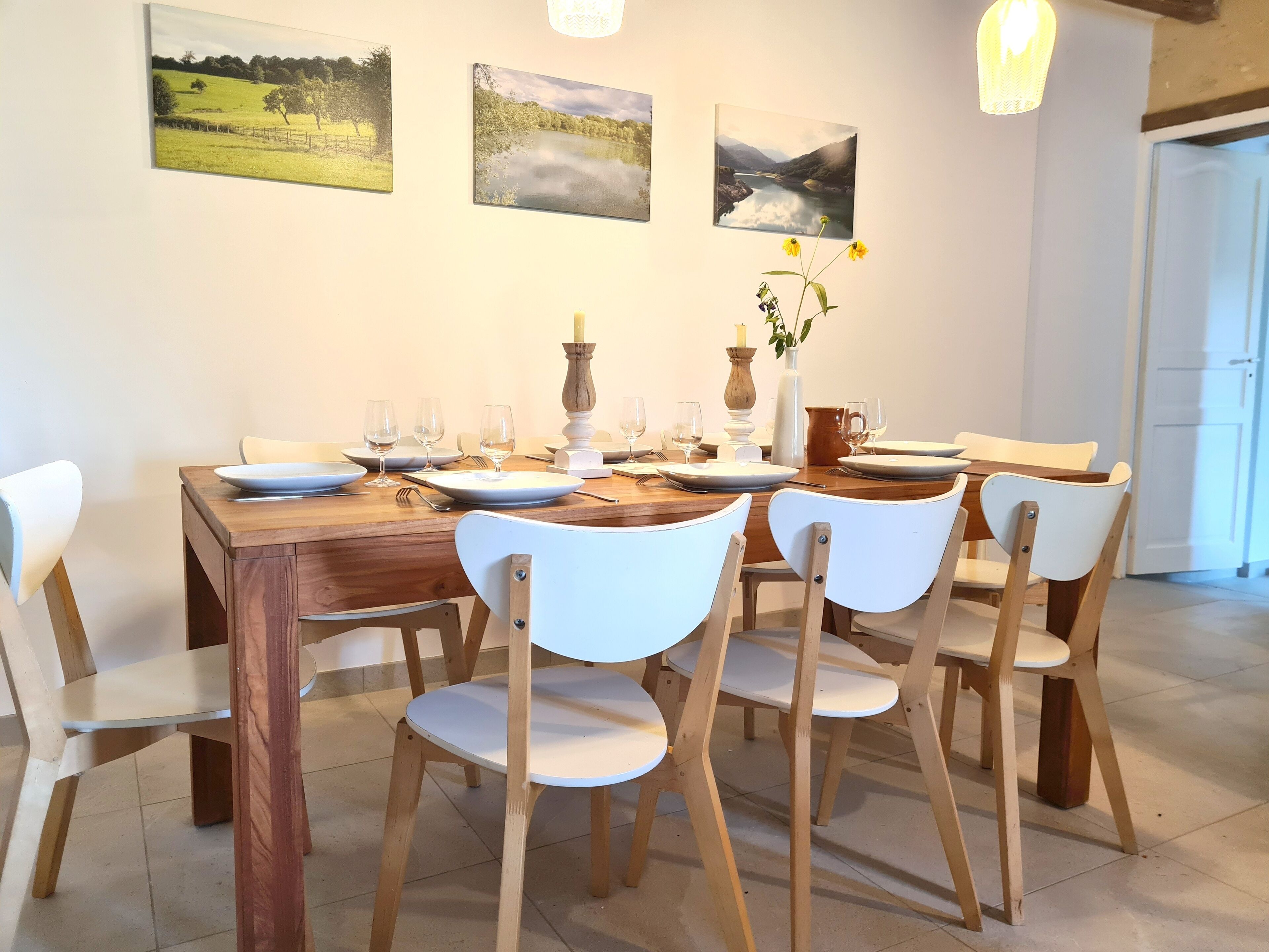 A dining table set with plates, glasses, and cutlery, surrounded by white chairs.