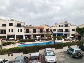 A hotel courtyard with a swimming pool, outdoor seating, and parked cars. - Luxurious 3-Bed Villa, Modern Decor, communal Pool (Kato Paphos)