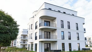 Un moderno edificio residenziale a più piani con balconi, ampie finestre e un prato ben curato.