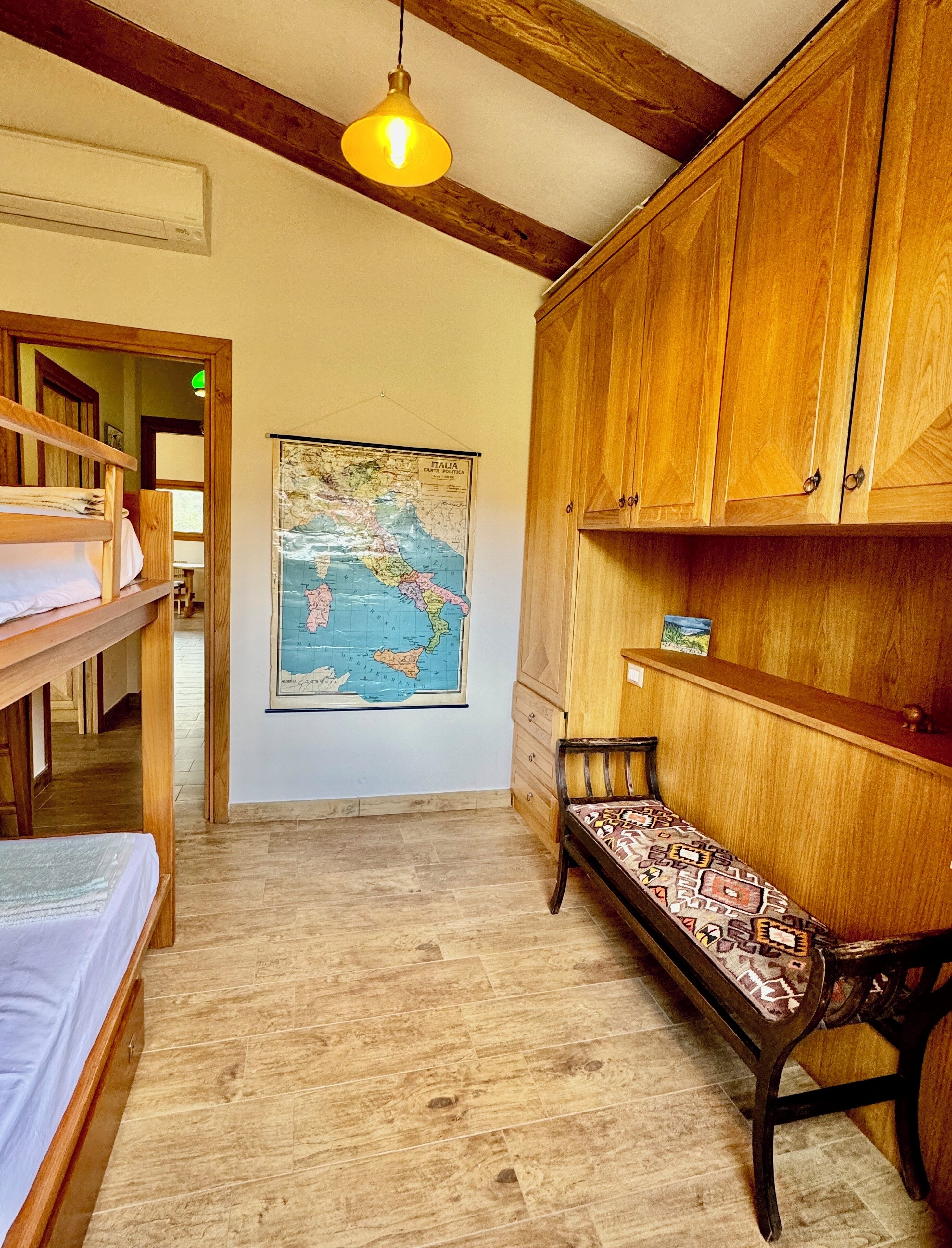 A room with wooden bunk beds, a wooden bench, a map on the wall, and a hanging light fixture.