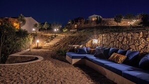 A nighttime outdoor seating area with a stone wall, a sofa with cushions, and a staircase leading up. - THE HIDEOUT Exclusive residence surrounded by nature, near Porto Rotondo (Sardegna)