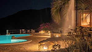 A nighttime pool area with a stone pathway, a palm tree, and a building with warm lighting. - THE HIDEOUT Exclusive residence surrounded by nature, near Porto Rotondo (Sardegna)