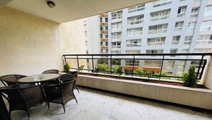 Uma varanda com mesa e cadeiras, vista de um prédio residencial e guarda-corpo.