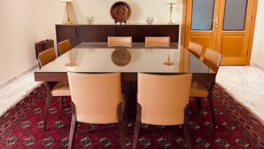Uma sala de jantar com uma mesa de vidro, seis cadeiras, um armário de madeira escura e um tapete vermelho estampado.