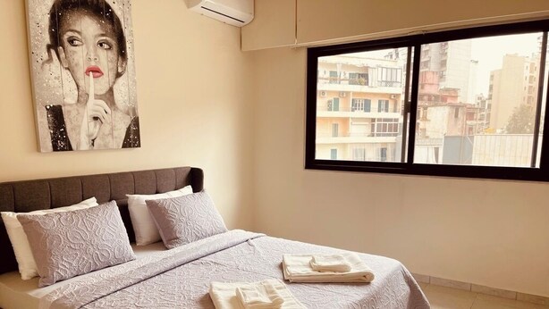 Quarto com uma cama grande, janela com vista para a cidade e um quadro na parede.