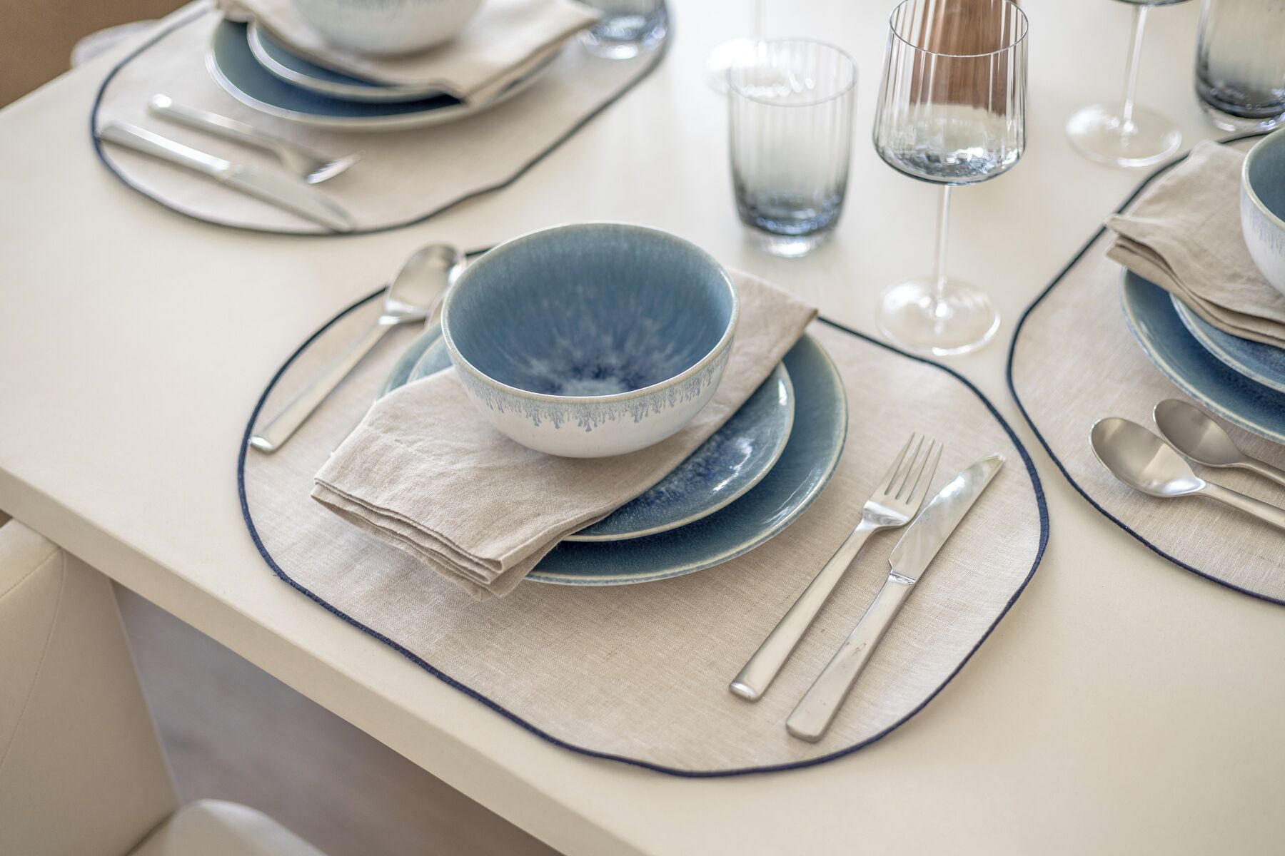 A neatly set dining table with blue and white plates, bowls, and cutlery, arranged on beige placemats.