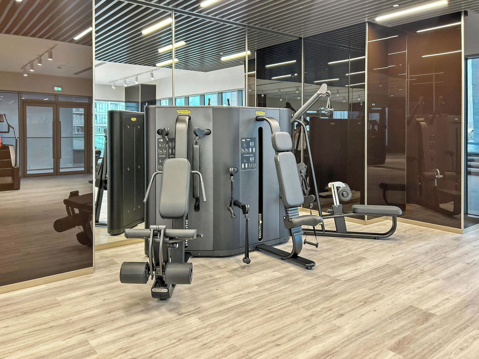A modern gym with exercise equipment, wooden flooring, and large windows.