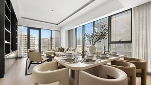 Uma sala de jantar moderna com uma mesa grande posta para seis pessoas, rodeada por seis cadeiras. A sala possui janelas amplas com vista para o horizonte da cidade.