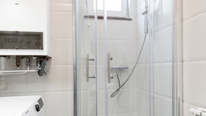 Ein modernes Badezimmer mit einer gläsernen Duschkabine, einer Waschmaschine und einer weißen Fliesenwand.
