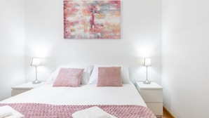 Ein modernes Schlafzimmer mit einem großen Bett, zwei Nachttischlampen und einer rosa, strukturierten Decke.