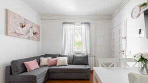 Ein modernes Wohnzimmer mit einem grauen Ecksofa, einem weißen Esstisch und einem großen abstrakten Gemälde an der Wand.