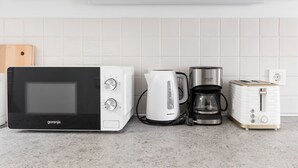 Eine Küche mit einer schwarzen Mikrowelle, einer weißen Kaffeemaschine, einem silbernen Kaffeekännchen und einem weißen Toaster.