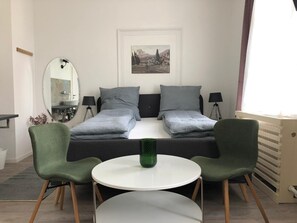 Et værelse med seng, to stole, et rundt bord, et spejl, en lampe og et billede på væggen.