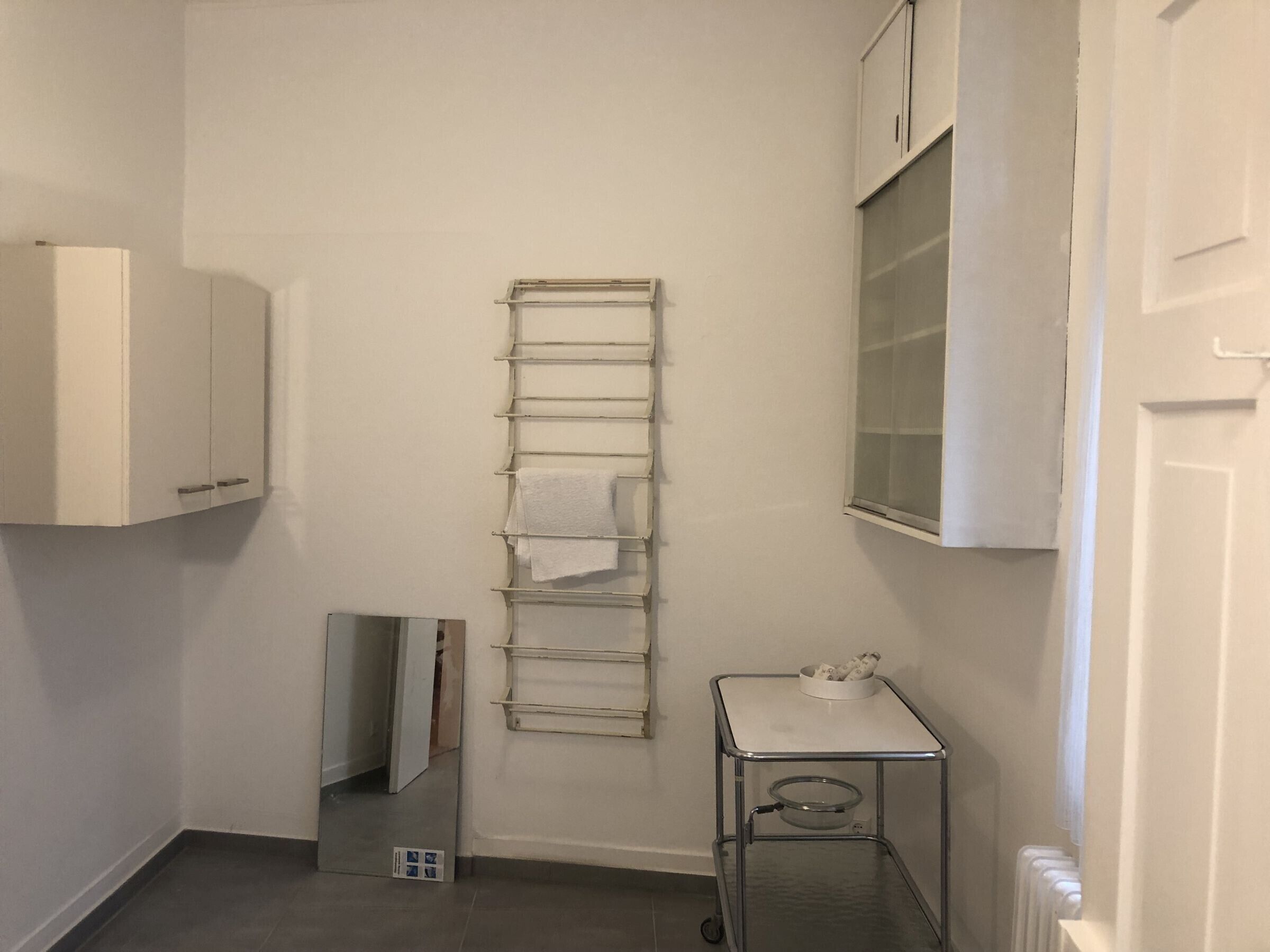 A small, clean bathroom with a towel rack, a cabinet, a radiator, and a small table with a bowl.