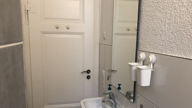 A bathroom with a white door, a sink with a mirror, and two soap dispensers on the wall. - Holiday Rooms Tübingen, 3 Bedrooms, 1 Living Room, Up to 8 Guests (Tübingen)
