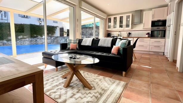 A modern living room with a glass dining table, a black leather sofa, and a view of a swimming pool. - Gîte Tango - Les Petites Écuries: Oasis au bord du canal du Midi (Marseillette)