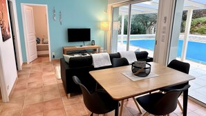 A modern living room with a sofa, TV, and a dining table with chairs. - Gîte Tango - Les Petites Écuries: Oasis au bord du canal du Midi (Marseillette)