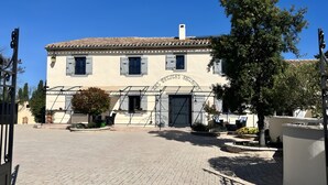 A building with a tiled roof, a central entrance, and a garden area with potted plants. - Gîte Tango - Les Petites Écuries: Oasis au bord du canal du Midi (Marseillette)