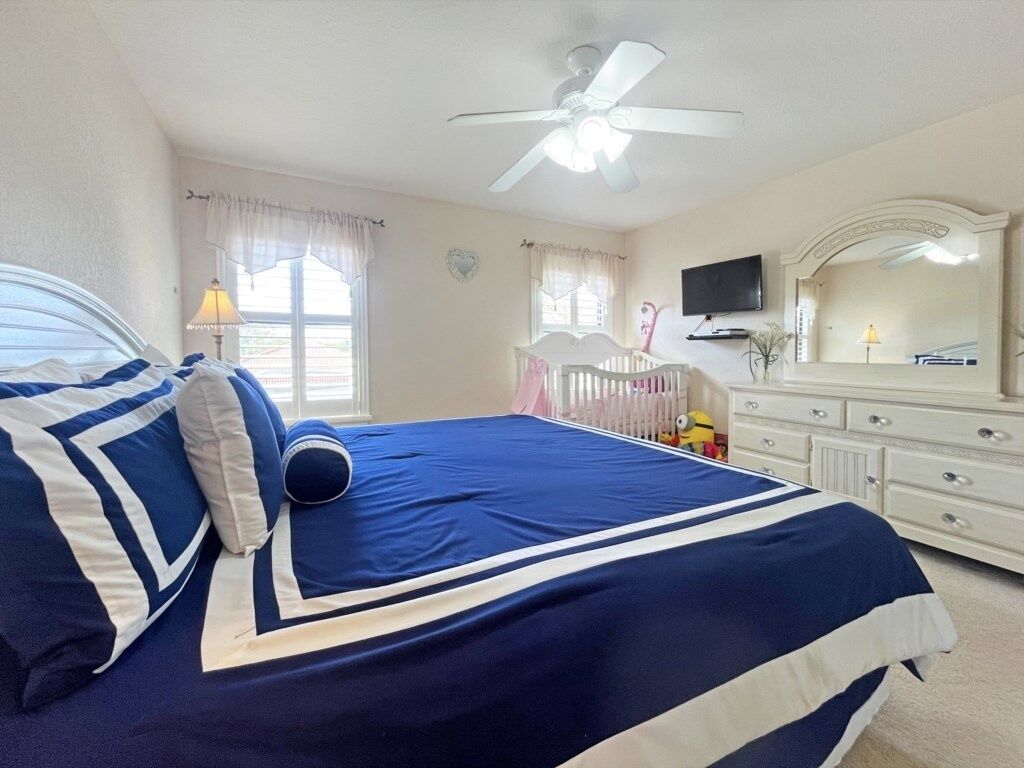Ein Schlafzimmer mit Bett, Kommode, Fernseher und Deckenventilator.