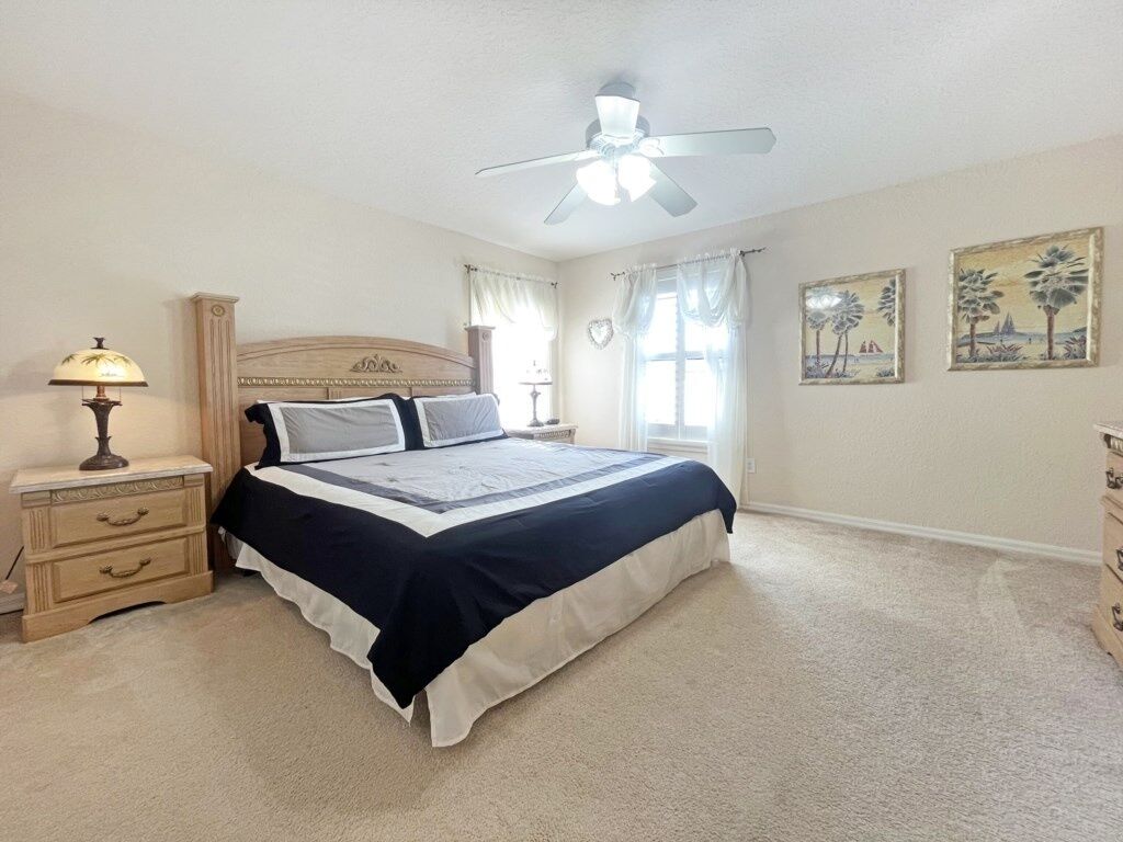 A bedroom with a bed, nightstands, a ceiling fan, and wall art.