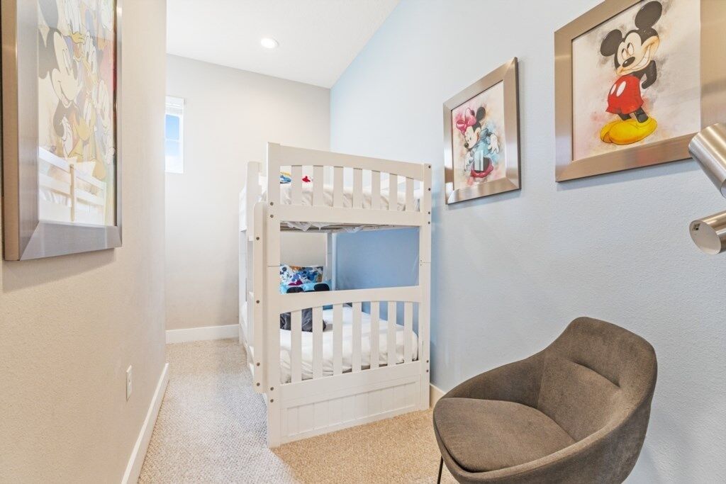 Une chambre d’enfant avec des lits superposés, des œuvres d’art de Disney encadrées et un fauteuil rembourré.