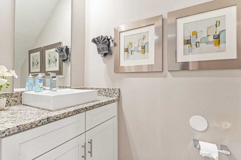 A bathroom with a white sink, granite countertop, and framed artwork on the wall.